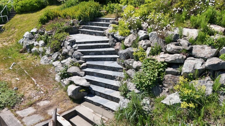 Flagstone steps winding up a hillside between natural boulders and planting