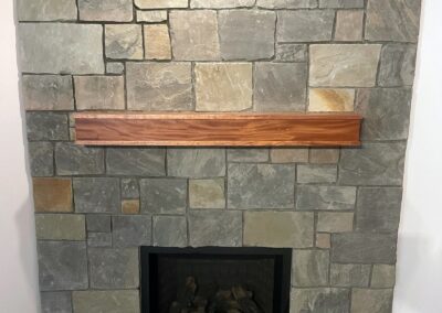 Custom natural stone fireplace with a modern wood mantel, featuring an ashlar stone pattern, installed in a residential home in Victoria, BC.