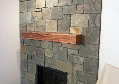 Custom natural stone fireplace with a modern wood mantel, featuring an ashlar stone pattern, installed in a residential home in Victoria, BC.