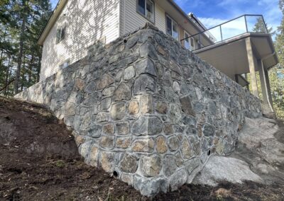 Custom-built stone retaining wall for an elevated home, providing structural support and durability, installed by Orca Masonry in Victoria, BC.