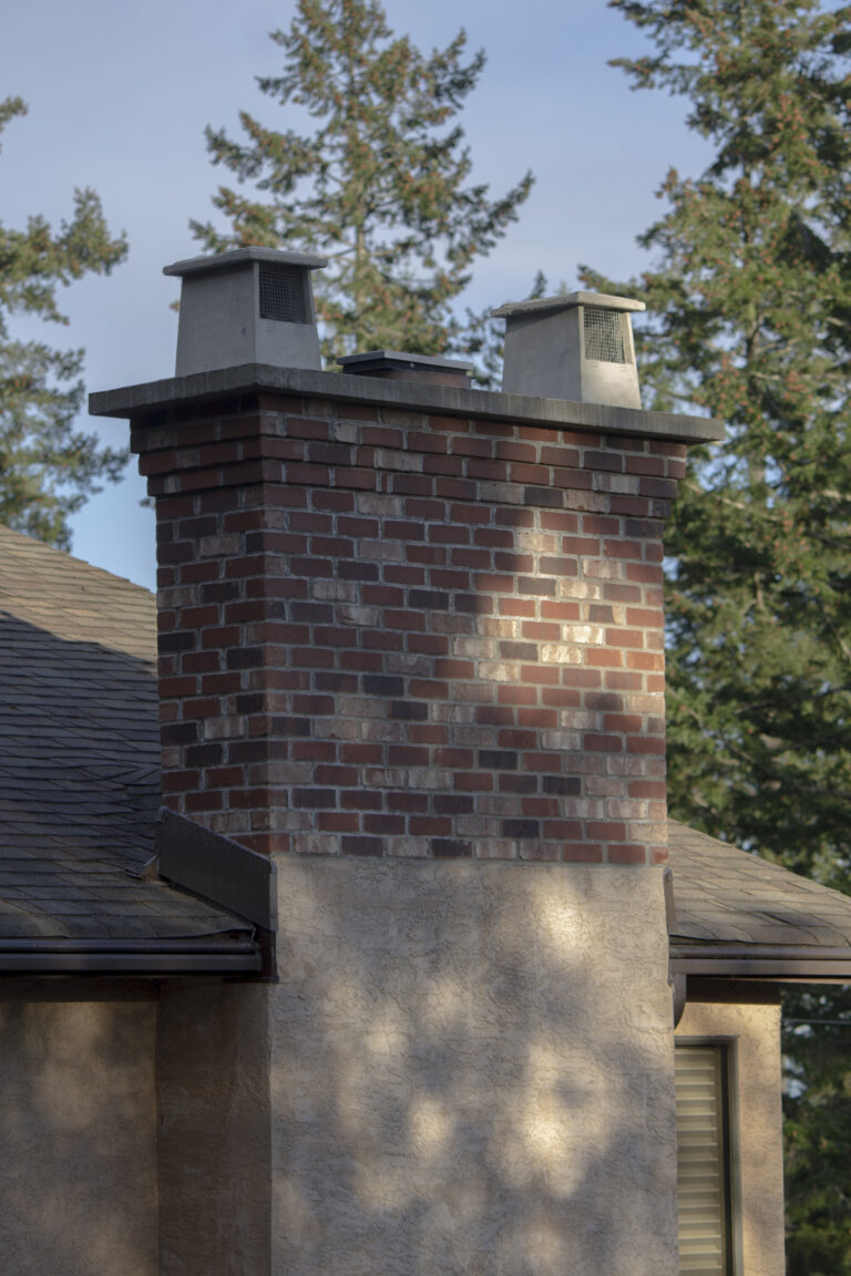 Red and dark mixed brick chimney with two caps, rising from a stucco chase