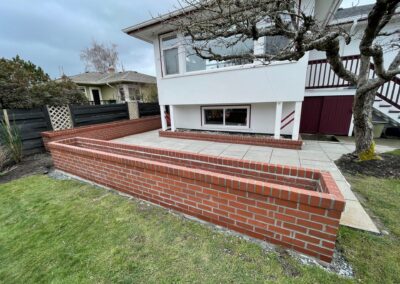 Custom red brick planter wall with patio in Greater Victoria residential backyard.