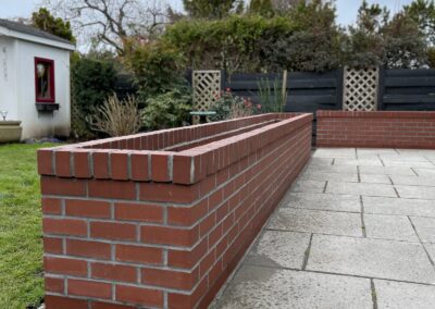 Custom red brick planter wall with patio in Greater Victoria residential backyard.