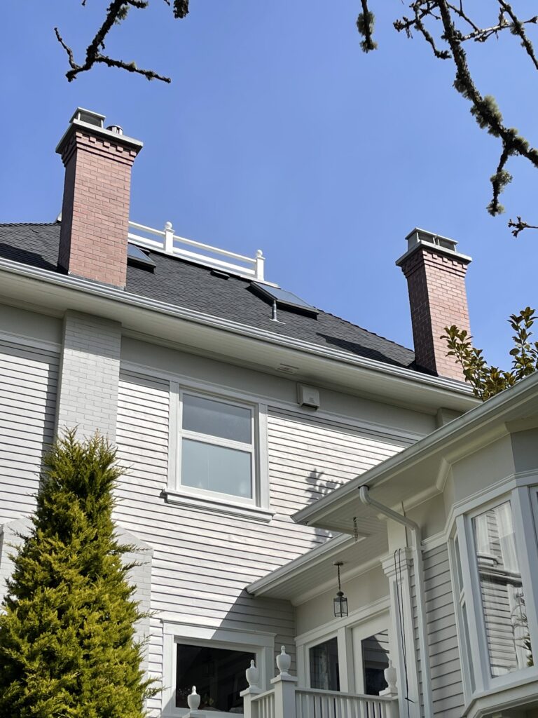 Two red brick chimneys with corbelled tops on a tall grey heritage home