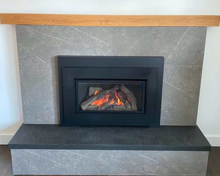 Gas fireplace insert in a grey tile surround with a raised black hearth and wood mantel