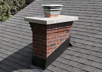 Traditional red brick chimney featuring corbel detailing and a concrete crown with rain cap protection.