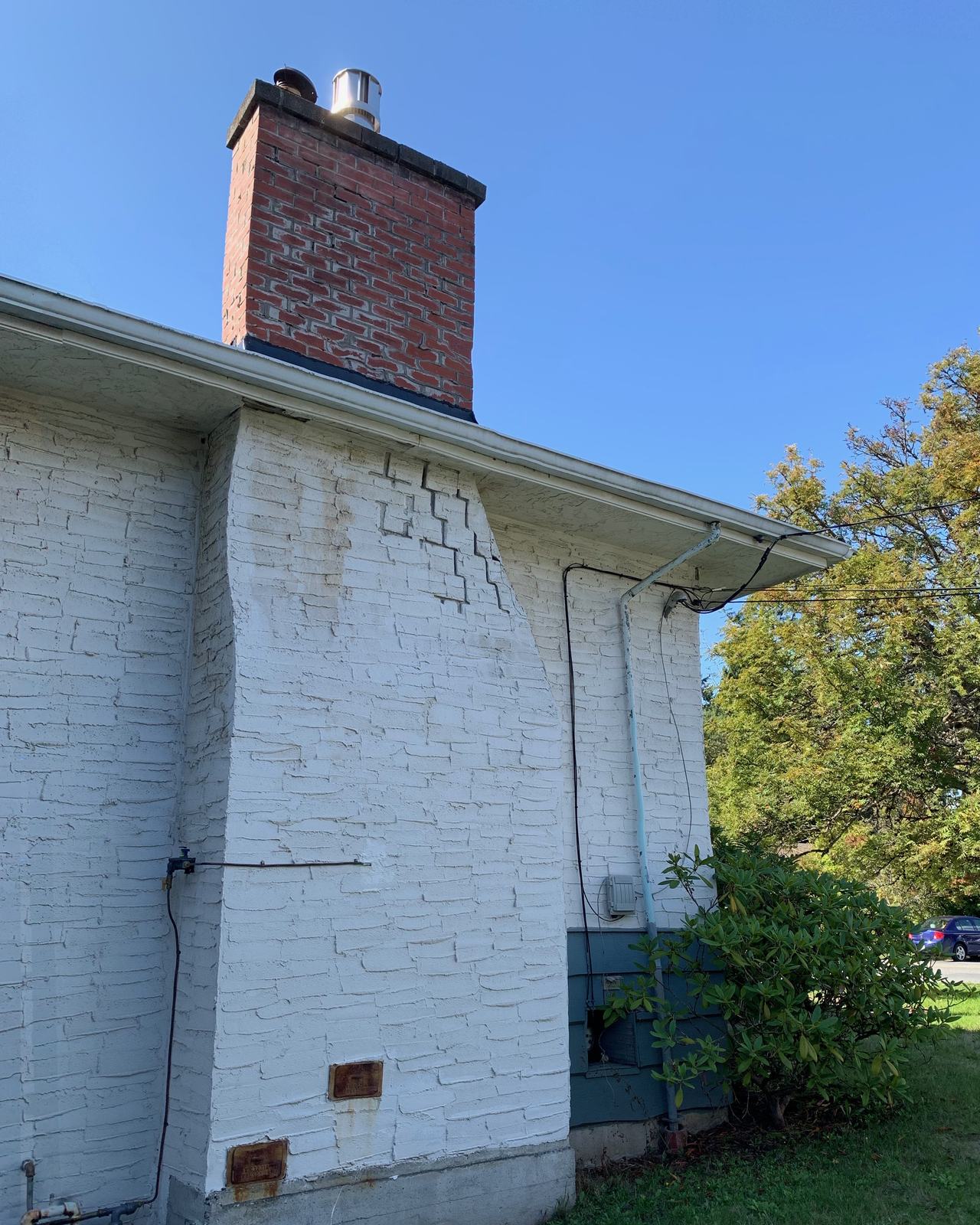 Chimney before the rebuild: old red brick stack above a white painted brick wall