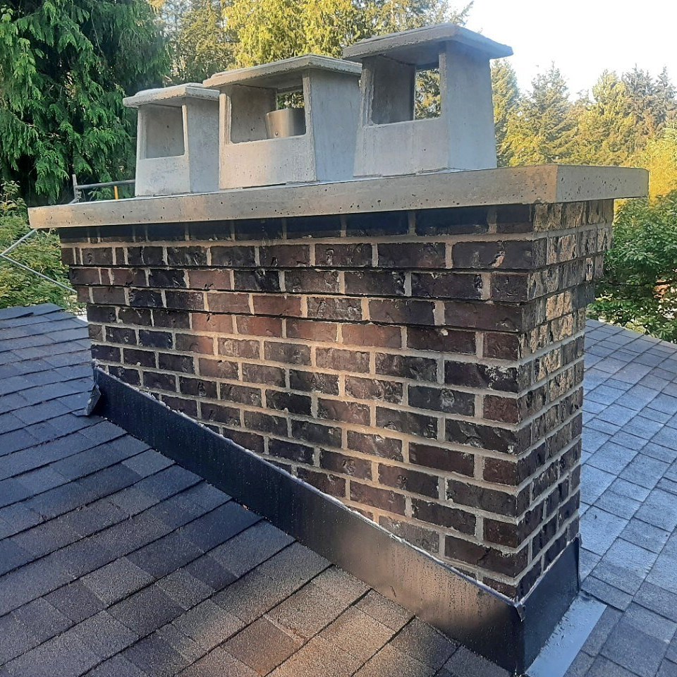 Dark brick chimney with a concrete crown and screened flue covers on a shingle roof