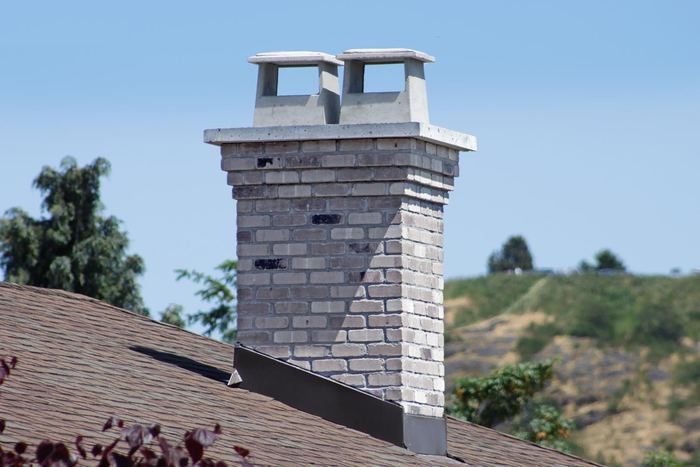 Light grey and buff brick chimney with a concrete crown and caps, a green hillside behind