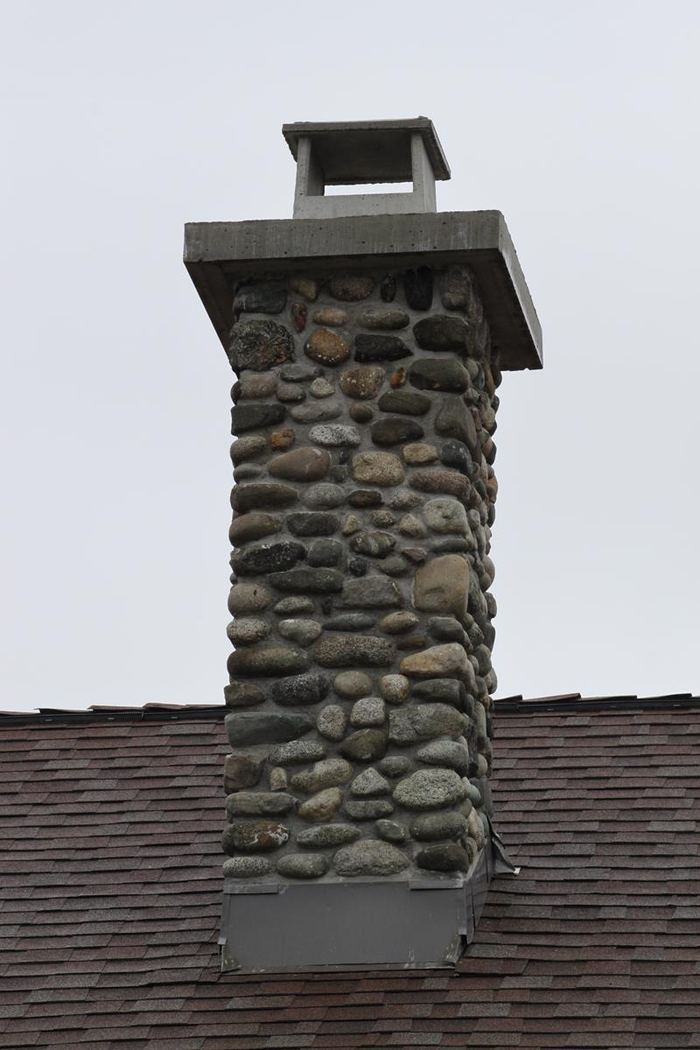 Rounded river rock chimney with a concrete crown and cap
