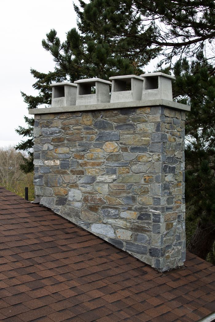 Natural stone chimney in mixed grey and tan stone with a concrete crown and four flue caps