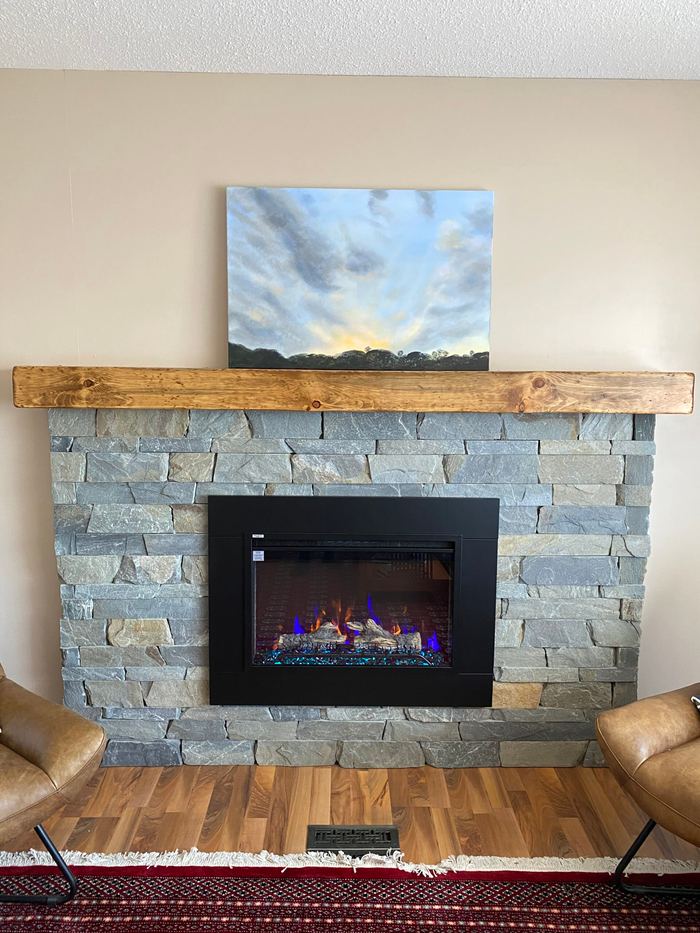 Grey ledgestone fireplace with a gas insert, a rustic timber mantel and a painting above