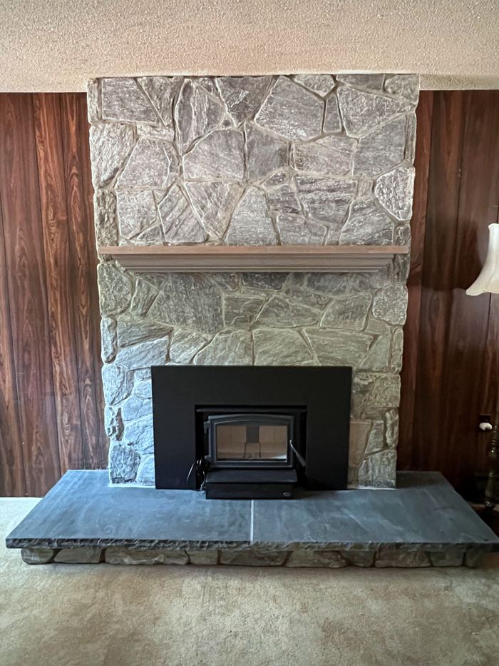 Natural stone fireplace with a wood-burning insert, wood mantel and a wide stone hearth
