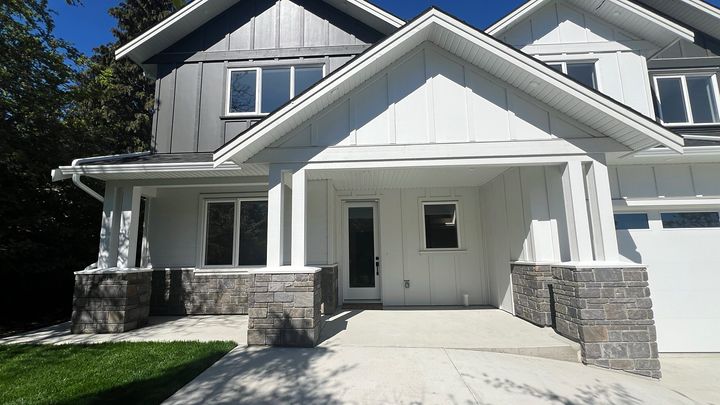 New-build front porch with stone veneer column bases and wainscot above a broom-finish concrete entry