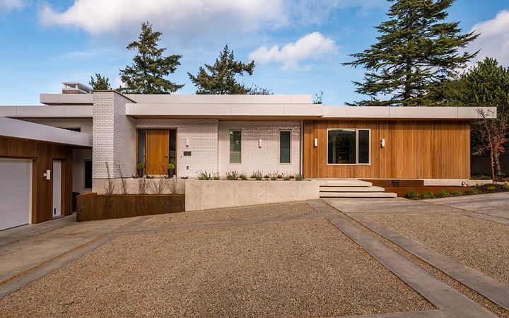 Modern home behind a courtyard of gravel panels and concrete bands, with a board-formed planter wall and floating steps