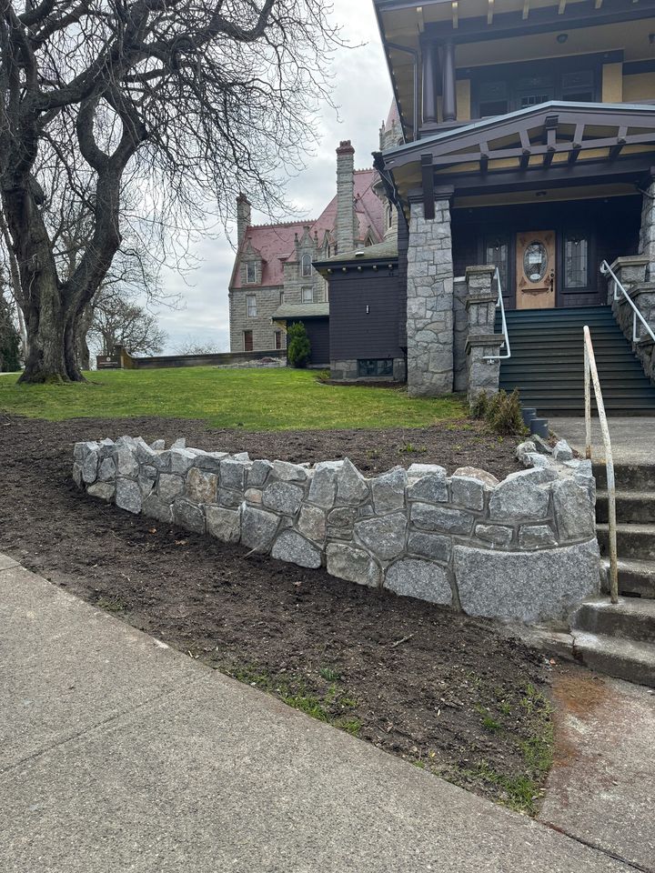 Granite rubble garden wall beside the front steps of a heritage home, with Craigdarroch Castle beyond