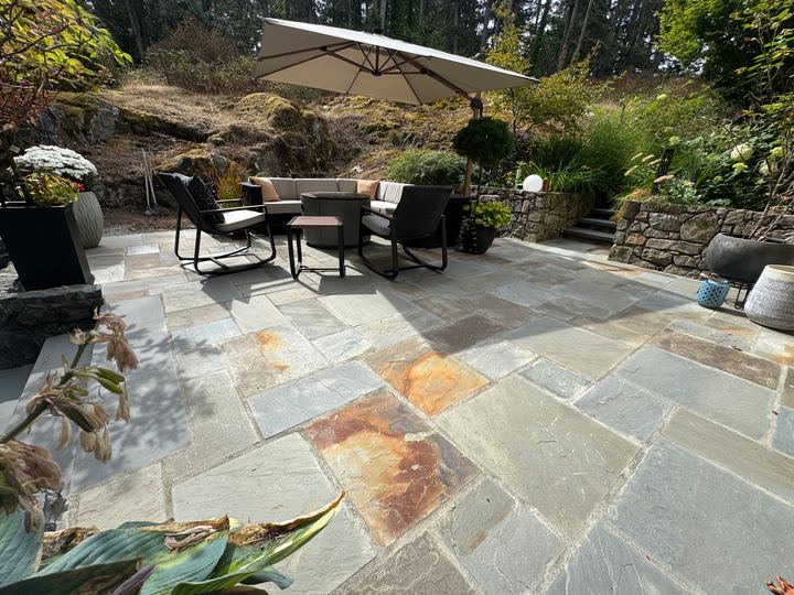 Wide bluestone patio with outdoor seating and an umbrella, natural stone walls behind