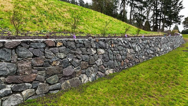 Long fieldstone retaining wall running along a grassy berm