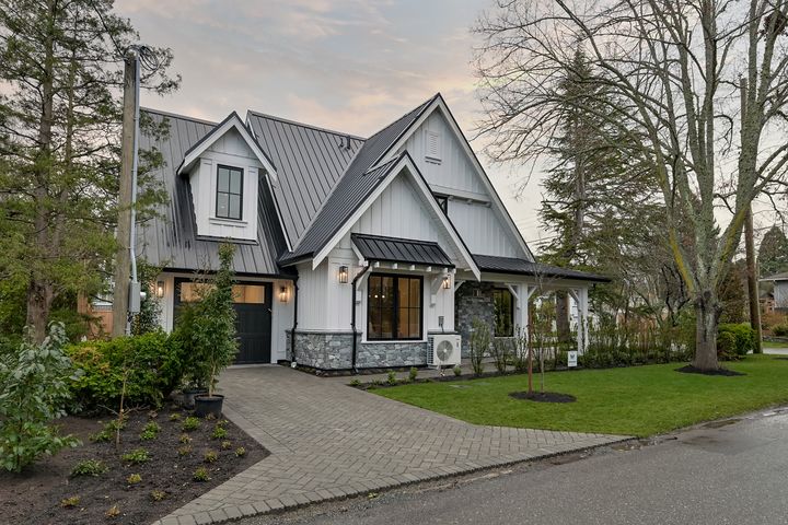 Herringbone paver driveway curving past a white farmhouse with stone veneer wainscot at dusk