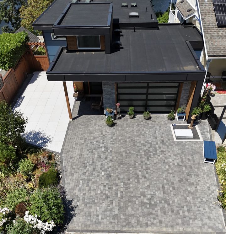 Drone view of a grey paver courtyard and driveway in front of a modern garage
