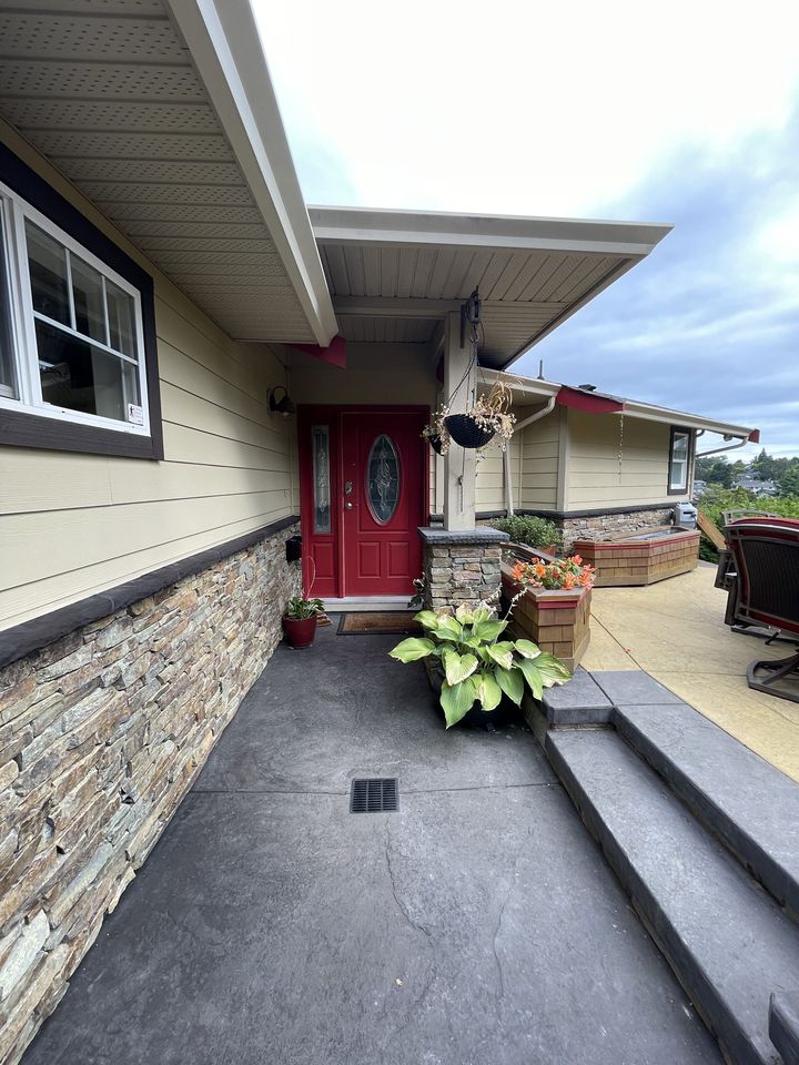 Ledgestone veneer wainscot and entry column beside stamped concrete steps and walkway to a red front door