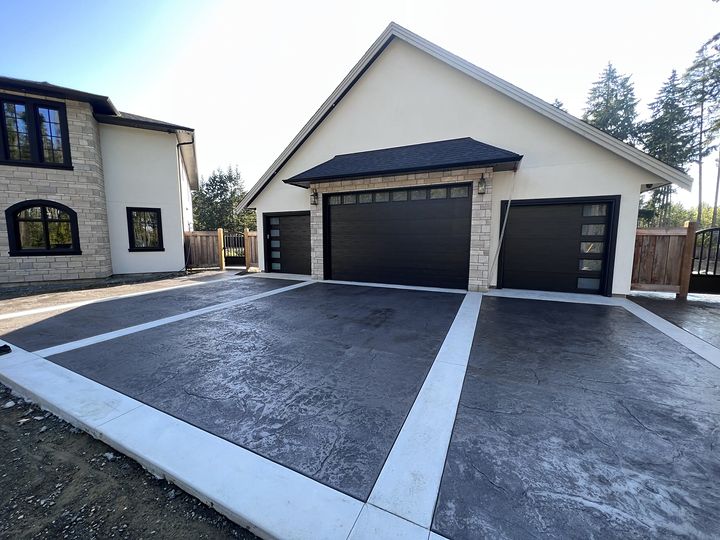 Charcoal stamped concrete driveway with bright white borders in front of a three-car garage