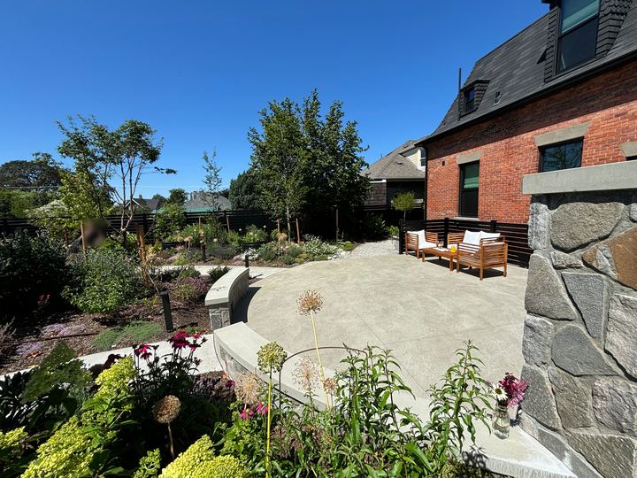 Wide concrete patio with stone-faced seat walls and outdoor seating beside a brick house