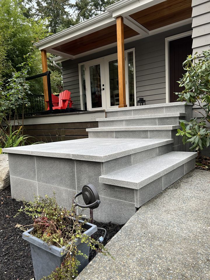 Wide grey granite entry steps and landing beside a porch with red chairs