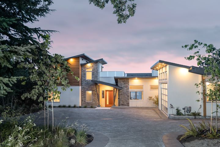 Wide dusk view of a paver courtyard and driveway in front of a modern home