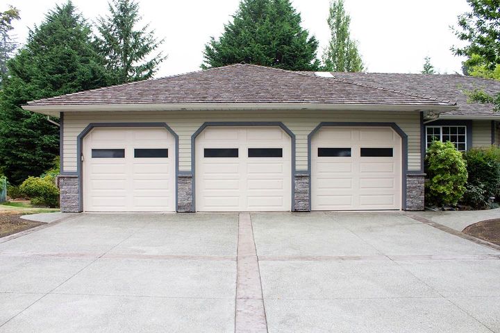 Exposed aggregate driveway with stamped borders in front of a three-car garage with stone veneer columns