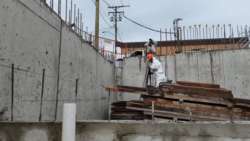 Crew member spraying membrane on a tall foundation wall from the footing
