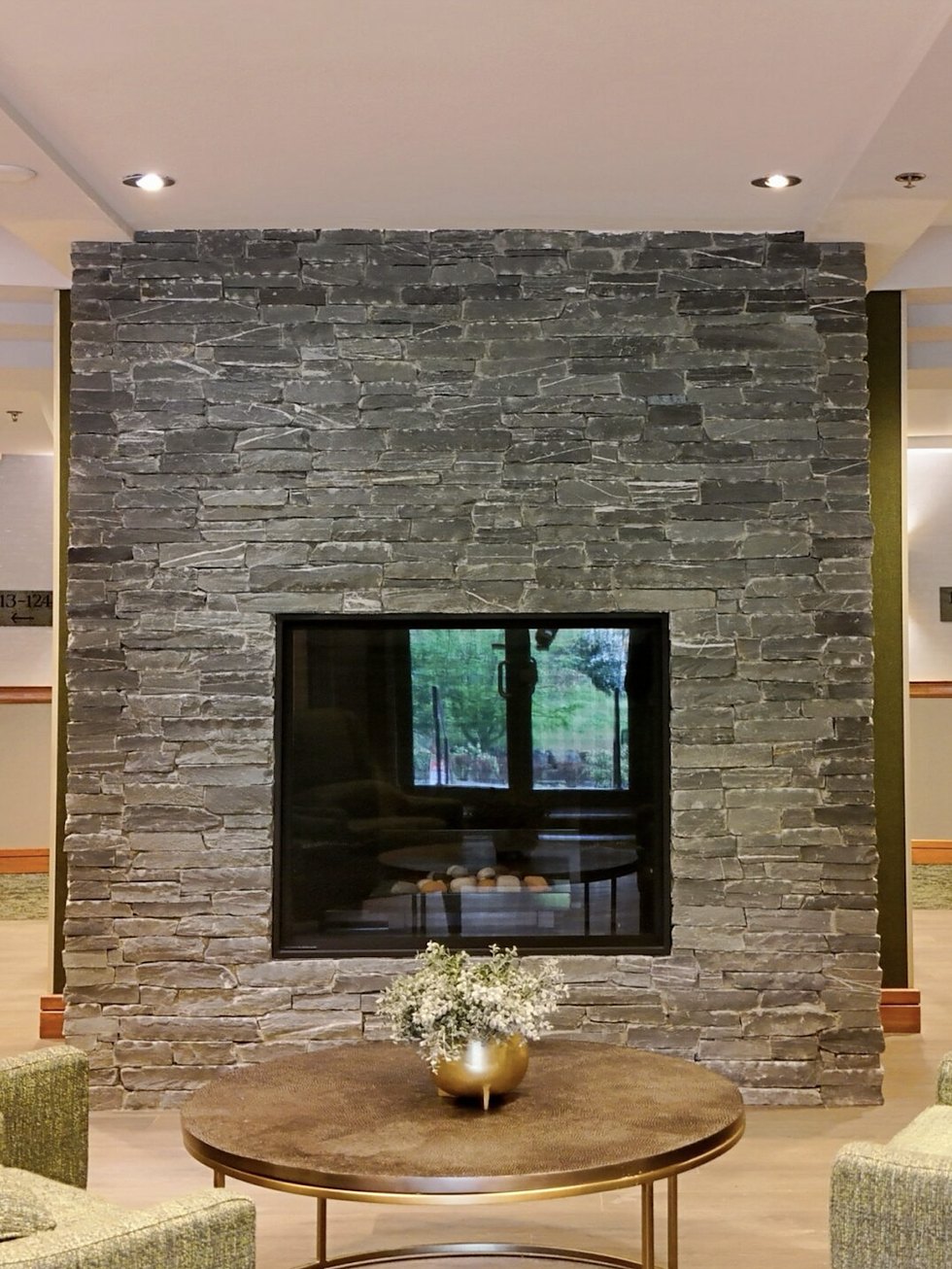 Double-sided stacked stone fireplace in a lounge, built by Orca Masonry