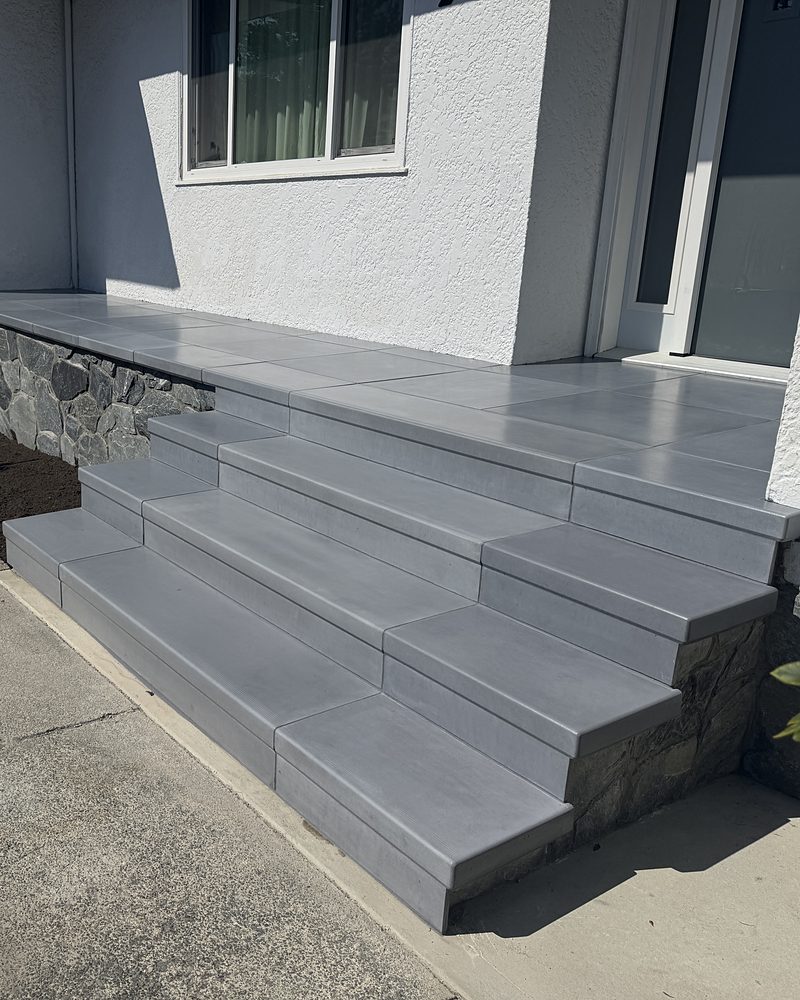 The same front entry after StepClad: wide grey treads, a tiled landing and stone veneer on the sides