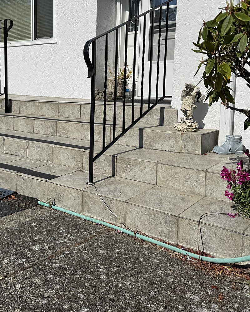 Old grey tiled front steps and landing with black metal railings, before StepClad