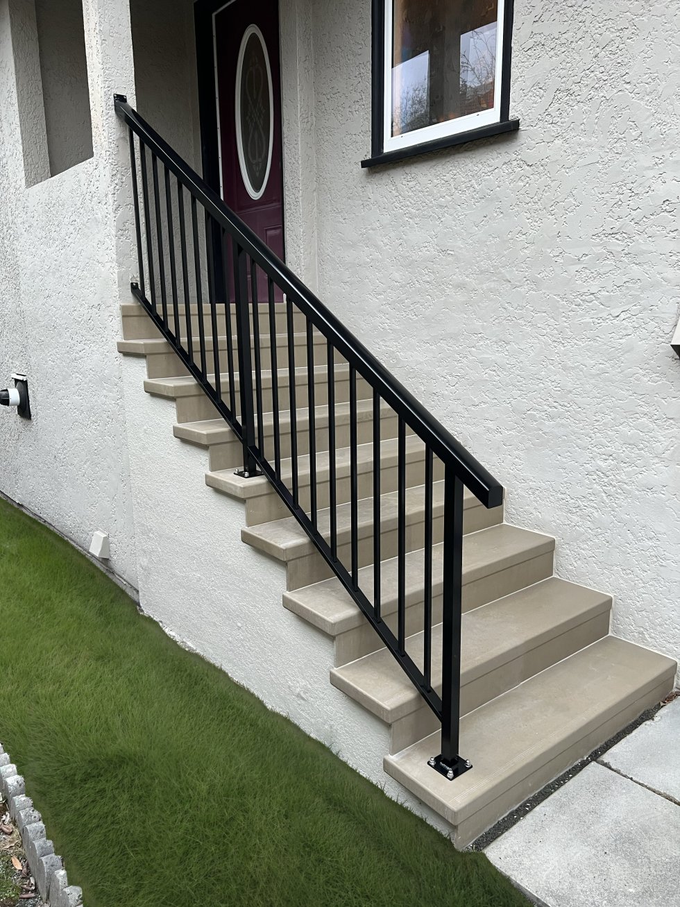 New concrete steps with black railing beside a stucco home