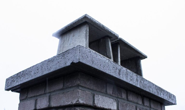 Grey brick chimney with a thick concrete crown and twin caps