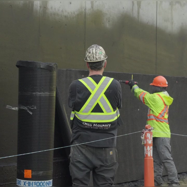 Orca crew fastening drain mat on a commercial foundation wall