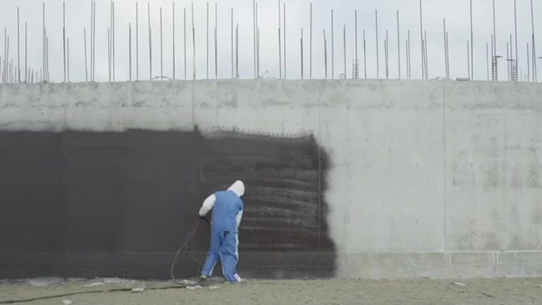 Crew member spraying NaturaSeal waterproofing membrane onto a commercial foundation wall